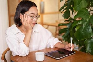 Young artist drawing on digital tablet, using graphic pen, drinking coffee in cafe and scatching smth photo