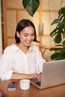 Smiling female manager, freelancer or student sitting with laptop in cafe and working, typing on computer photo