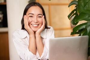 Beautiful young woman with happy smile, sitting in cafe with laptop, studying remotely, working online from distance photo