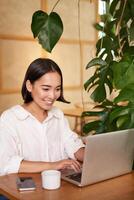 Smiling female manager, freelancer or student sitting with laptop in cafe and working, typing on computer photo