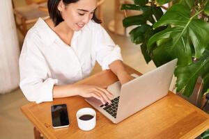 Working woman in cafe, using laptop, studying remotely, freelancing from restaurant, drinking coffee photo