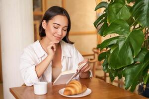 Smiling beautiful girl with a book, reading with thoughtful smirk, thinking of something, drinking coffee in cafe photo
