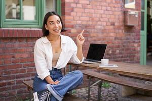 Enthusiastic asian woman, pointing at upper right corner, showing advertisement, news on banner, looking impressed and intrigued by smth photo