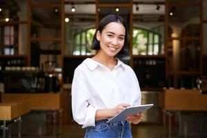 Young asian waitress, cafe manager working with tablet and graphic tablet photo