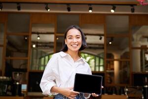 sonriente asiático hembra gerente, café dueño, demostración tableta pantalla, demostrando algo en su dispositivo foto