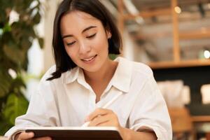 Portrait of asian girl drawing on digital tablet, scatching and doodling with graphic pen, sitting in cafe and smiling photo