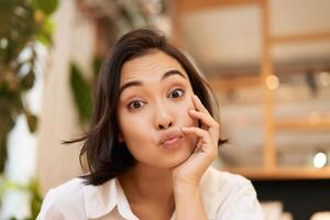 Close up portrait of funny young asian woman, sitting in cafe, chatting lively, smiling at camera photo