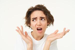 Portrait of confused, puzzled young woman, gasping, looking disappointed and frustrated, shrugging shoulders, posing over white background photo