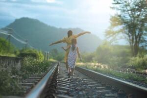 madre y linda hija caminando en el ferrocarril en el tiempo de día. contento familia caminando en el ferrocarril en contra el antecedentes de montañas y verdor. foto