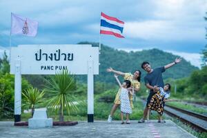 Happy family taking pictures together at Pang Puai Railway Station against a background of green mountains and trees. photo