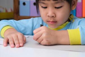 alegre niña feliz dibujando con lápices de colores sobre papel sentado en la mesa en su habitación en casa. creatividad y desarrollo de la motricidad fina. foto