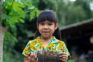 Little girl shows saplings grown in recycled plastic bottles. Recycle water bottle pot, gardening activities for children. Recycling of plastic waste photo