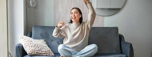 Happy and carefree girl singing and listening to music on smartphone app, using mobile phone as microphone, sitting on sofa photo