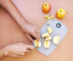 Close up male hands cut an apple into slices. Top view of preparing fruits over kitchen table. photo