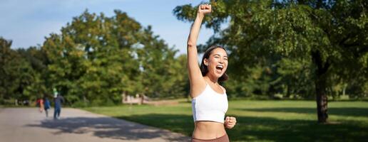Hooray, victory. Smiling asian girl triumphing, celebrating achievement, running till finish, shouting from excitement photo