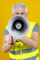mature worker screaming into megaphone isolated on yellow background photo