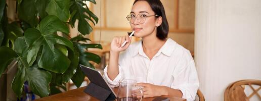Young artist drawing on digital tablet, using graphic pen, drinking coffee in cafe and scatching smth photo