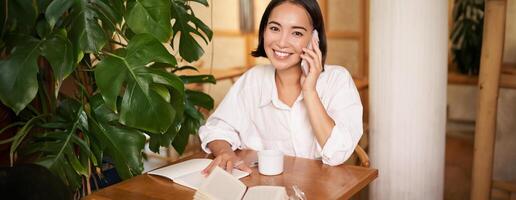 Smiling woman talking on mobile, answer phone call and looking happy, sitting in cafe photo