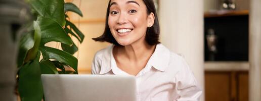 Beautiful young woman with happy smile, sitting in cafe with laptop, studying remotely, working online from distance photo