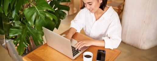 Working woman in cafe, using laptop, studying remotely, freelancing from restaurant, drinking coffee photo