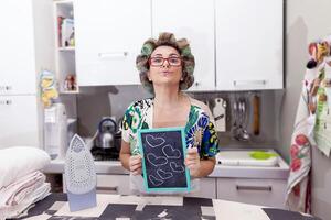 mature housewife woman with curlers shows a board with hearts photo