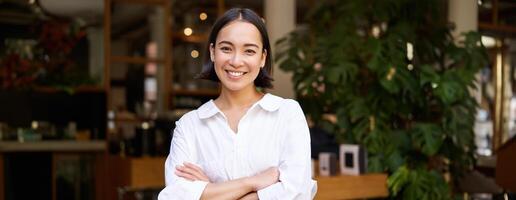 Portrait of smiling asian girl in white collar shirt, working in cafe, managing restaurant, looking confident and stylish photo