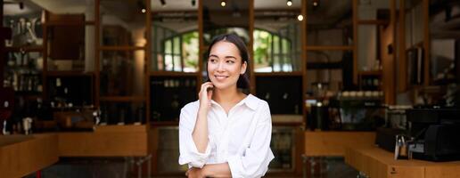 Portrait of young female entrepreneur, asian business owner or manager, sitting confident, smiling at camera with arms crossed photo