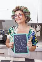 mature housewife woman with curlers shows a board with hearts photo