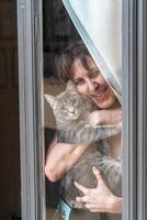 smiling woman embraces a cat looking from the window photo