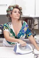 beautiful mature woman with curlers ironing clothes at home photo