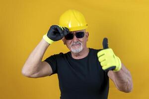 trabajador con guantes y casco demostración pulgar arriba en contra amarillo antecedentes foto