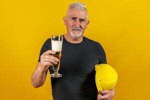 portrait of worker with yellow helmet drinking a beer on yellow background photo