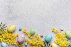 Pastel Easter Eggs and Yellow Mimosa Flowers on a Light Grey Background photo