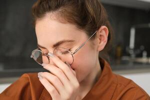 Close up portrait of romantic, cute young woman in glasses, covers her face, blushing and looking modest, laughing and smiling, giggling photo