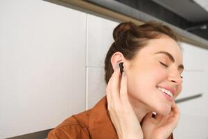 Close up portrait of woman smiling from sound quality in her wireless black earphones, listening to music in headphones, she has pleased face and eyes closed from satisfaction photo