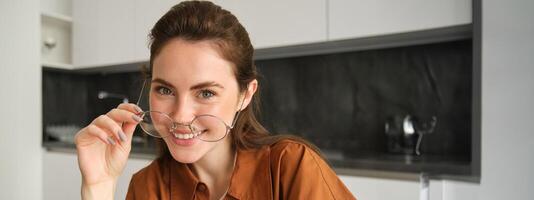 Close up portrait of carefree woman in glasses, sitting at home in kitchen, smiling and looking happy photo