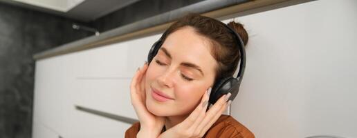 Portrait of beautiful young woman in headphones, relaxing, closes eyes from pleasure listening to music in earphones photo