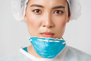 Covid-19, coronavirus disease, healthcare workers concept. Close-up of exhausted serious-looking asian female doctor take-off personal protective equipment, have skin damage from respirator photo