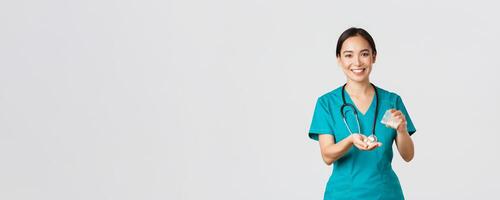 Healthcare workers, preventing virus, quarantine campaign concept. Smiling friendly asian female doctor, physician in scrubs, give patient medication from container, white background photo