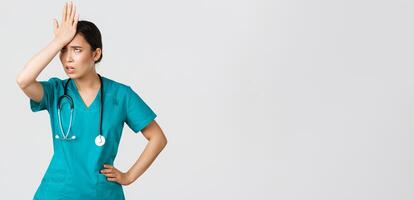 Covid-19, healthcare workers, pandemic concept. Annoyed and pissed-off asian female doctor in scrubs slap forehead, facepalm and eyeroll from someone stupid, tired standing white background photo