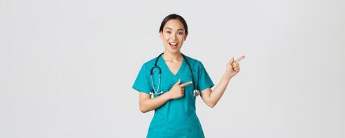 Covid-19, healthcare workers, pandemic concept. Glad smiling, beautiful asian doctor, female therapist in scrubs or nurse pointing fingers upper right corner, showing way to patient, white background photo