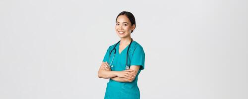 COVID-19, cuidado de la salud trabajadores, pandemia concepto. profesional seguro, sonriente asiático hembra doctor, enfermero en matorrales con estetoscopio para exámenes, cruzar brazos y Mira a cámara foto