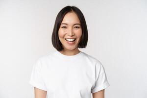 Close up portrait of young asian woman looking at camera, wearing t-shirt, smiling and looking happy, white background photo