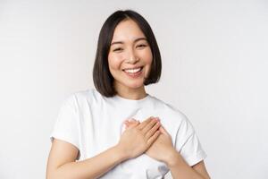 cerca arriba de sonriente coreano mujer participación manos en corazón, cuidado y amor concepto, sensación afecto, sensibilidad o reconfortante sentimiento, en pie terminado blanco antecedentes foto