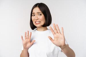 Disgusted asian woman rejecting smth, grimacing from dislike and aversion, stare with cringe, refusing offer, standing over white background photo