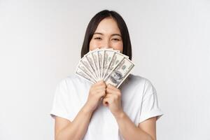 Portrait of smiling asian woman holding dollars money, concept of microcredit, finance and cash, standing over white background photo