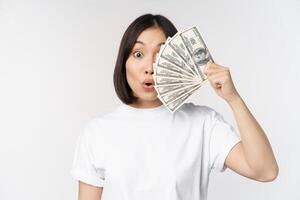 Happy asian girl holding money, cash near face, concept of microcredit and finance, white studio background photo