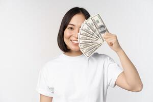 Portrait of smiling asian woman holding dollars money, concept of microcredit, finance and cash, standing over white background photo