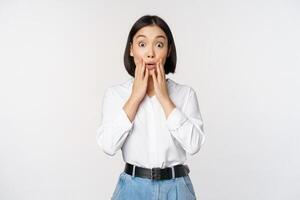 Portrait of surprised young office woman, asian businesswoman gasping amazed, saying wow, standing impressed of news against white background photo