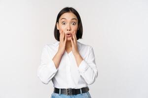 Image of asian female model looking surprised, staring amazed, reacting at surprise big news, standing over white background photo